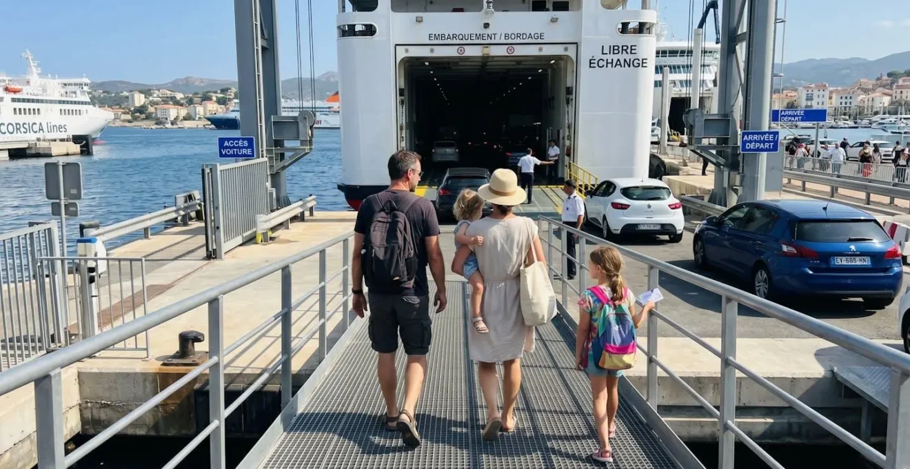 Une famille de quatre personnes vue de dos monte la passerelle d'embarquement d'un ferry moderne, leur voiture visible en arrière-plan sous un ciel méditerranéen ensoleillé